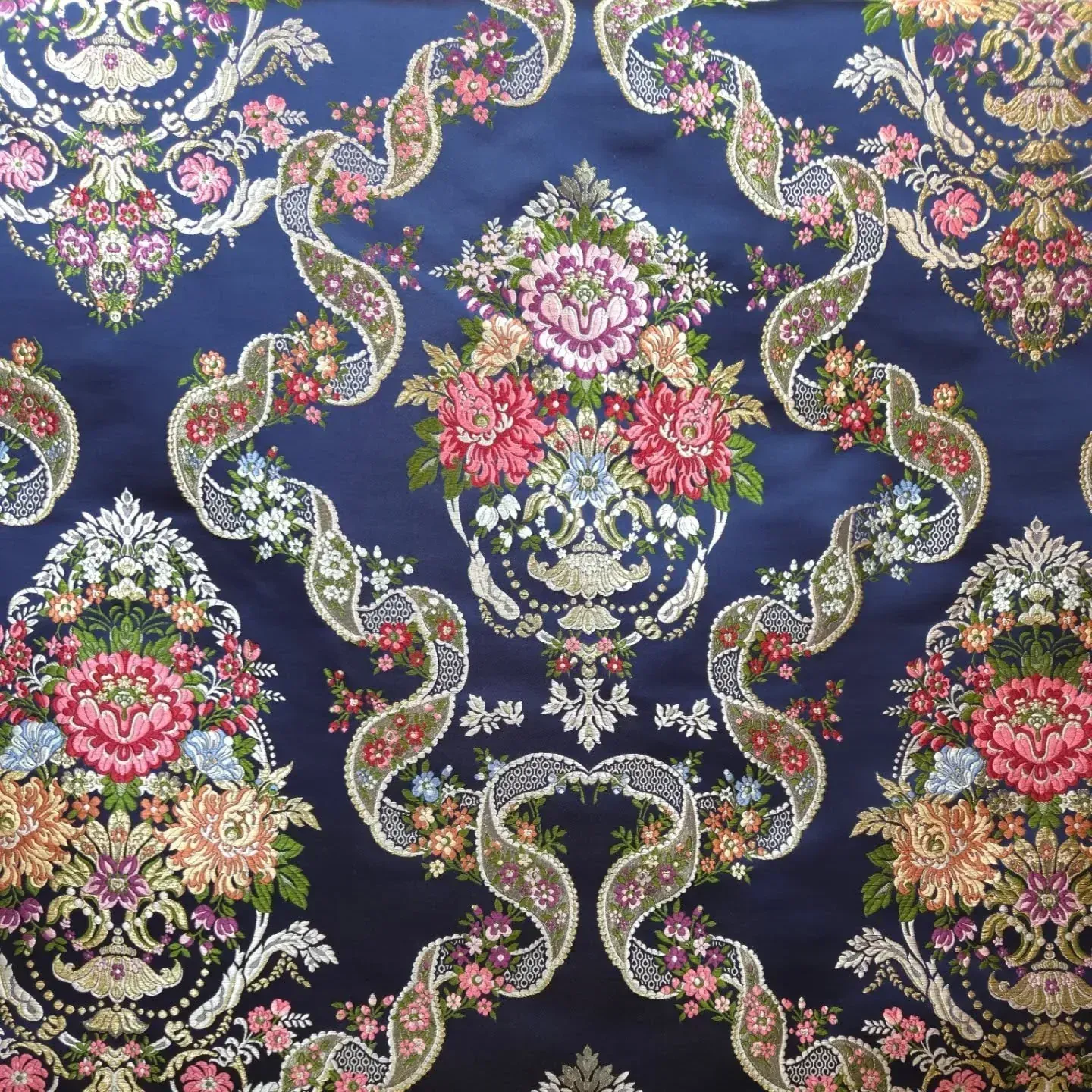 Tela azul oscuro con estampado floral y cintas adornadas en rosa, dorado y blanco.