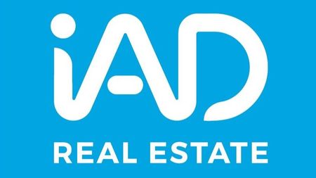 Logotipo blanco de “IAD” sobre fondo azul con el texto “REAL ESTATE” debajo.