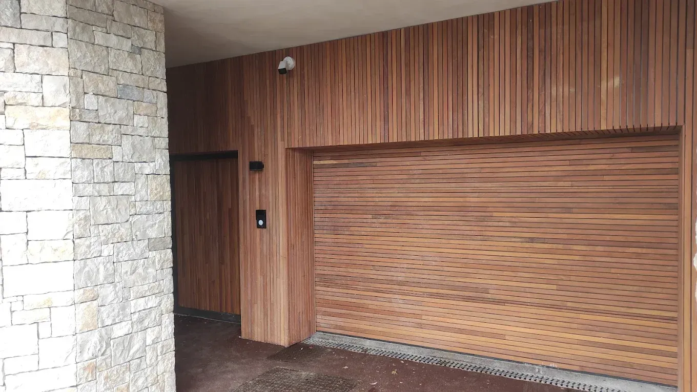 Extérieur du bâtiment avec murs lambrissés de bois, colonne en pierre et porte de garage fermée.