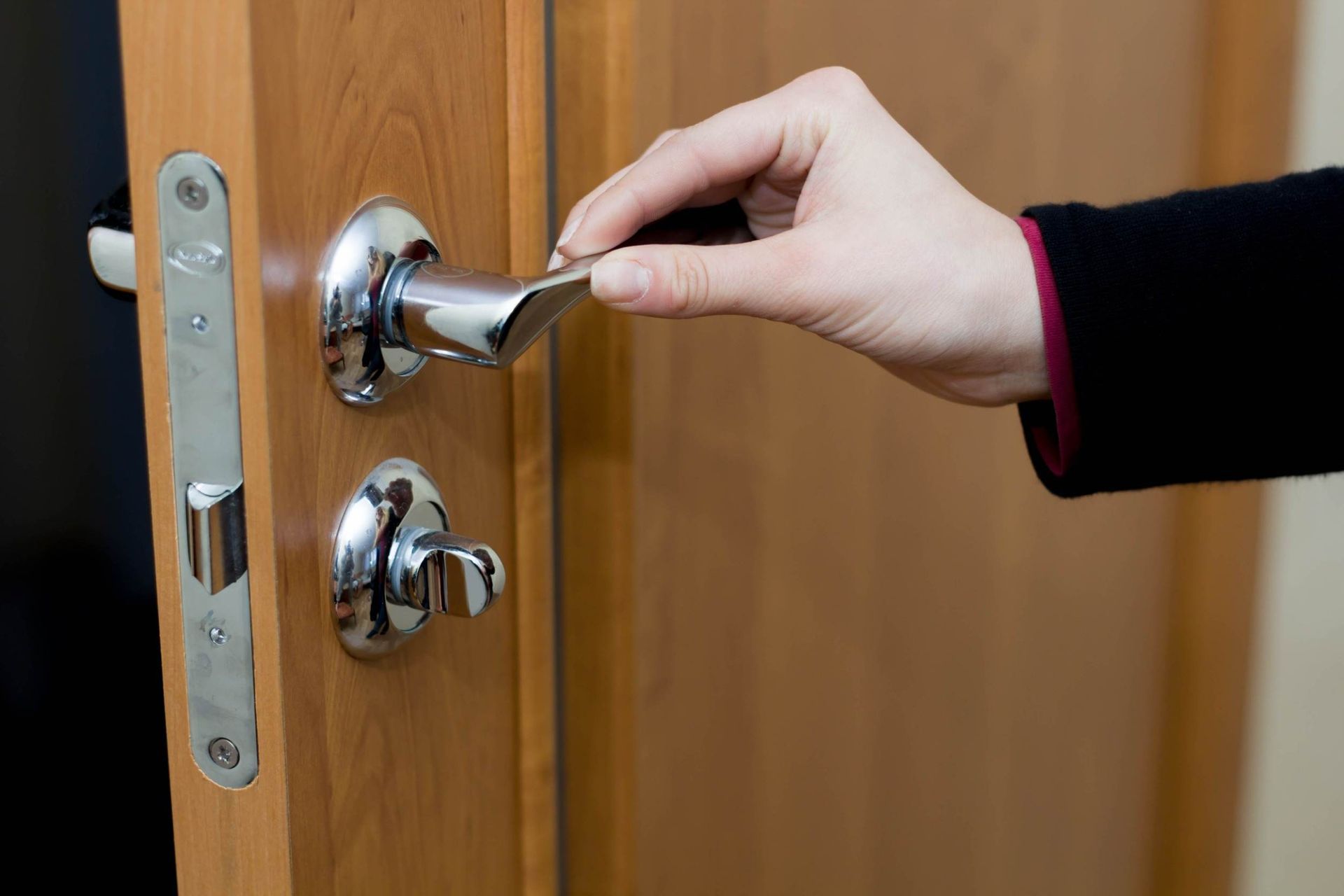 Una persona está abriendo una puerta de madera con una manija cromada.
