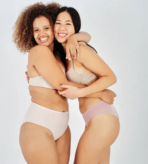 Dos mujeres en ropa interior se abrazan y sonríen.