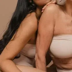 Dos mujeres están sentadas una al lado de la otra y una sostiene el hombro de la otra.
