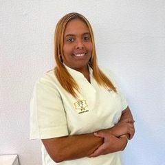 Una mujer que lleva gafas y reloj está de pie con los brazos cruzados y sonriendo.