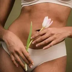 Una mujer en ropa interior blanca sostiene una flor en sus manos.