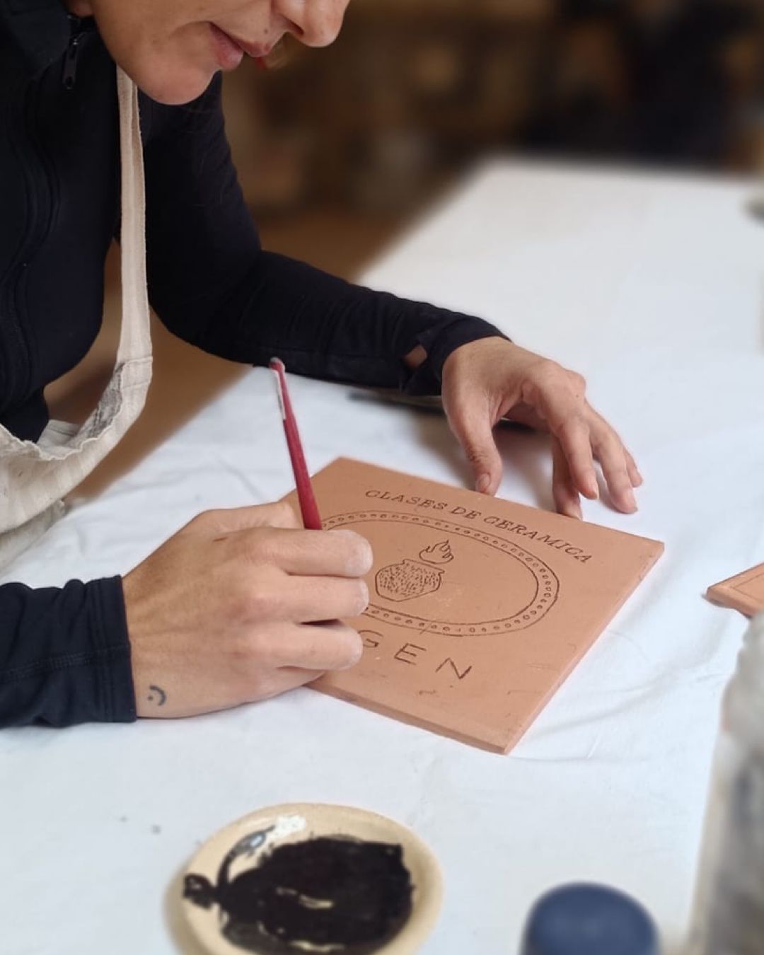 A person writing on a beige card with a red pencil,
sitting at a table with an inkwell nearby.