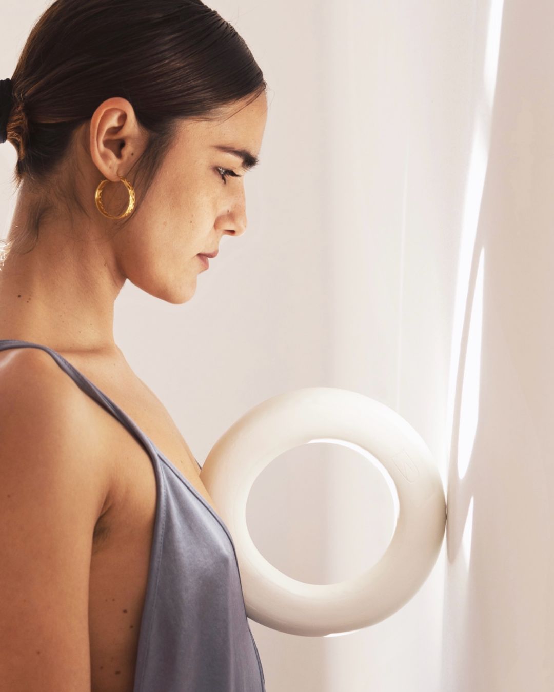 Mujer modelando arcilla en un torno de alfarero, hombre al fondo. Ambos llevan delantales en un taller.