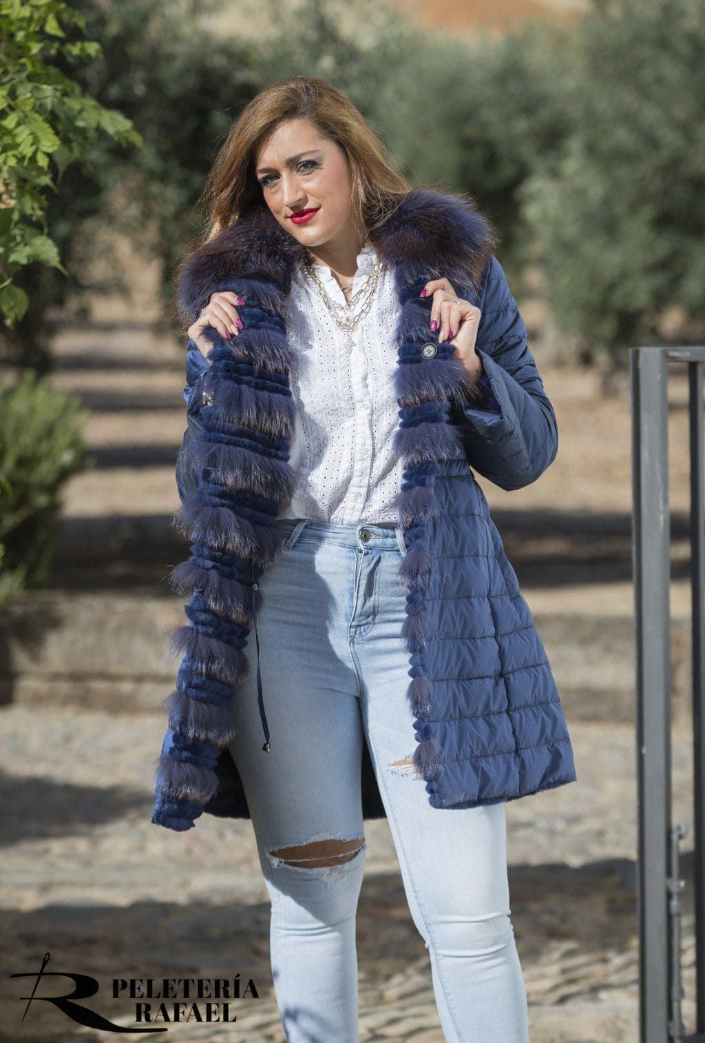 Mujer con abrigo azul y jeans rotos, sonriendo al aire libre.