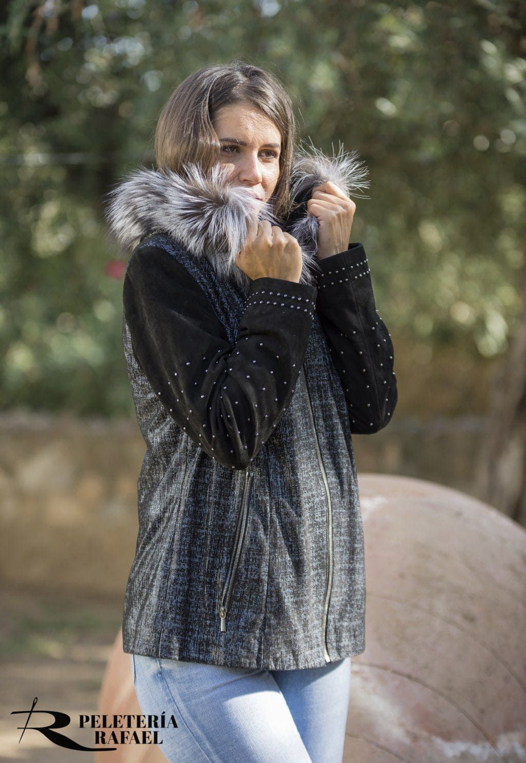 Mujer con chaqueta negra con cuello de piel, manos en alto, al aire libre.