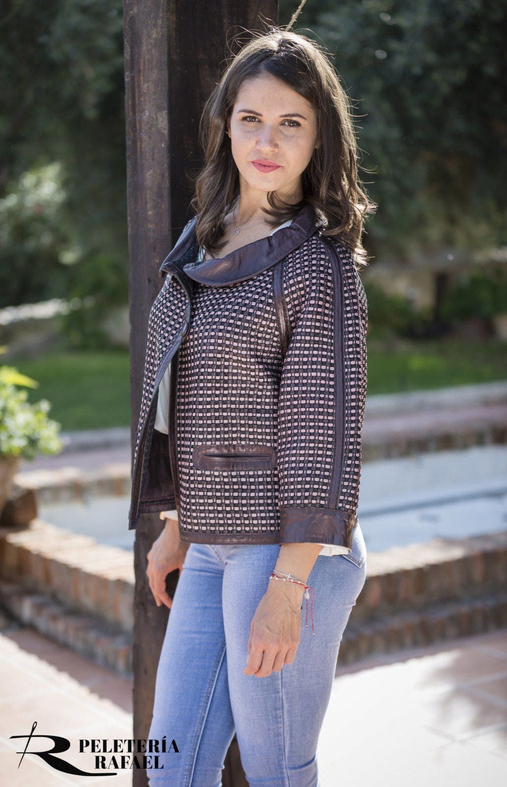 Mujer con jeans y chaqueta estampada, posando al aire libre.