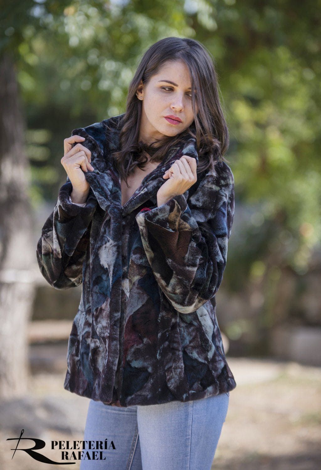 Mujer con un abrigo de piel estampado, pantalones vaqueros claros y mirando por encima del hombro al aire libre.