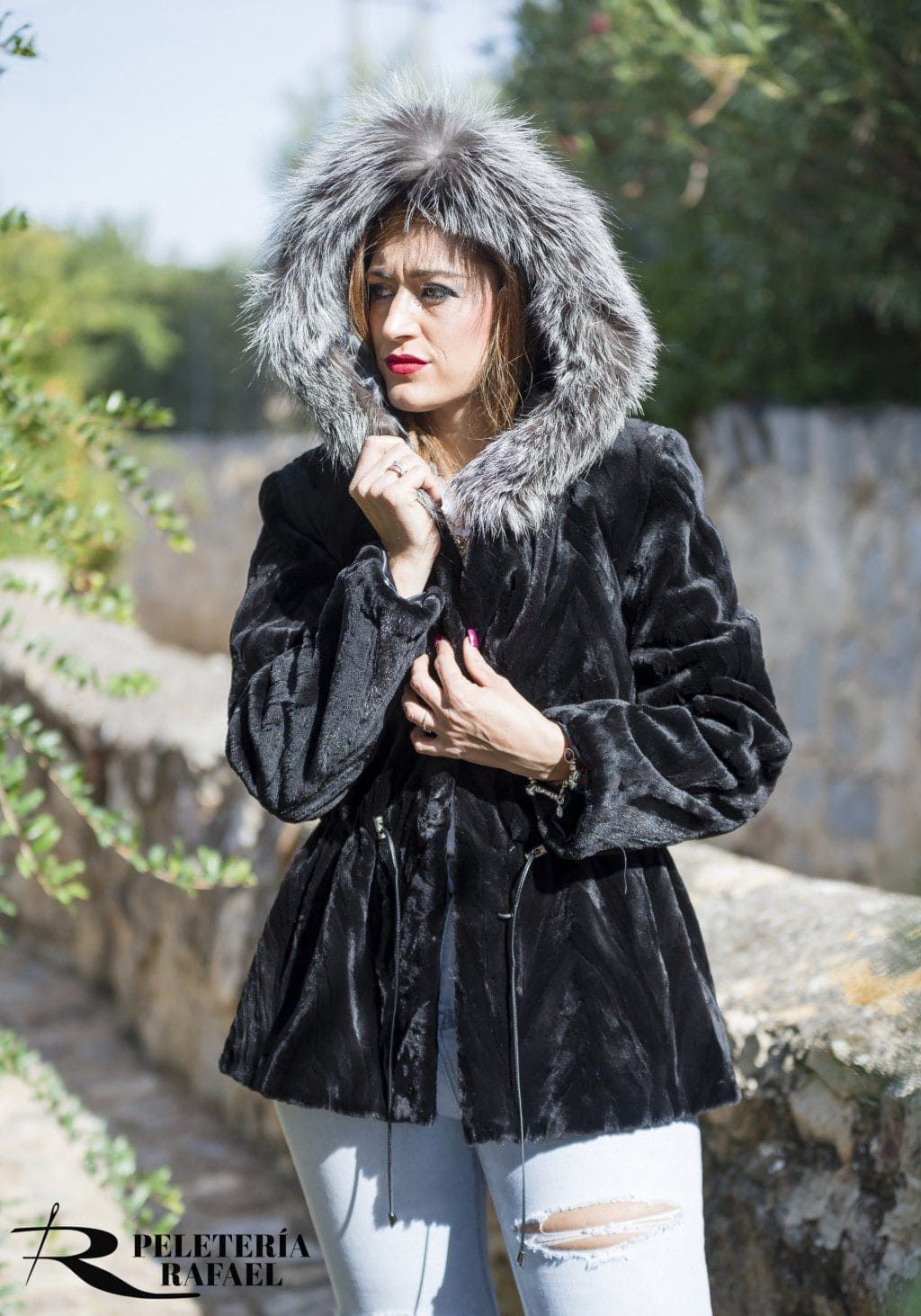 Mujer con un abrigo de piel negro y una capucha forrada de piel plateada, de pie al aire libre.