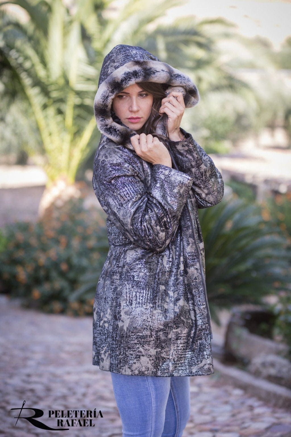 Mujer con abrigo con capucha, de pie al aire libre. El abrigo tiene una capucha forrada de piel. Ella se la está ajustando.