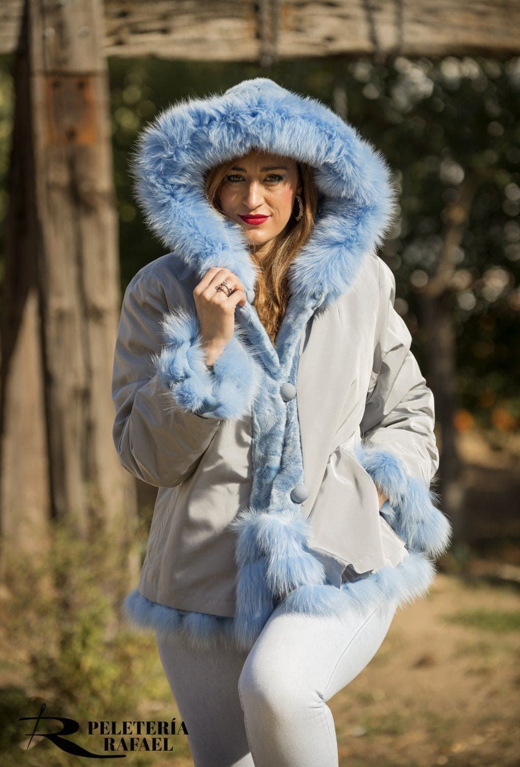 Mujer con un abrigo gris con ribete de piel azul y capucha, posando al aire libre.