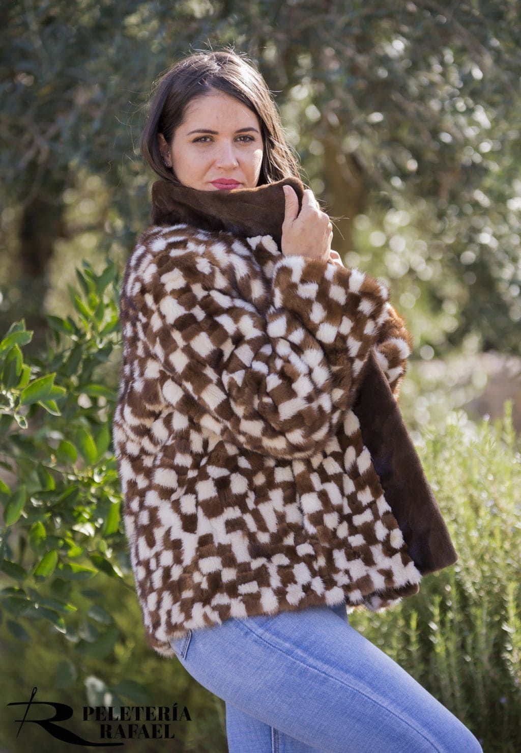 Mujer con abrigo de piel a cuadros marrones y blancos, vaqueros azules y mirando a la cámara. Escena al aire libre.