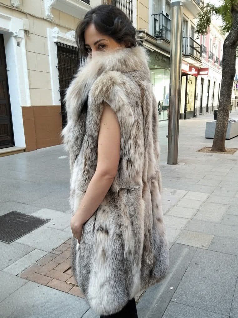 Dos mujeres con abrigos apoyadas en una farola negra al aire libre. Una viste de amarillo, la otra de rojo, ambas con vaqueros claros.