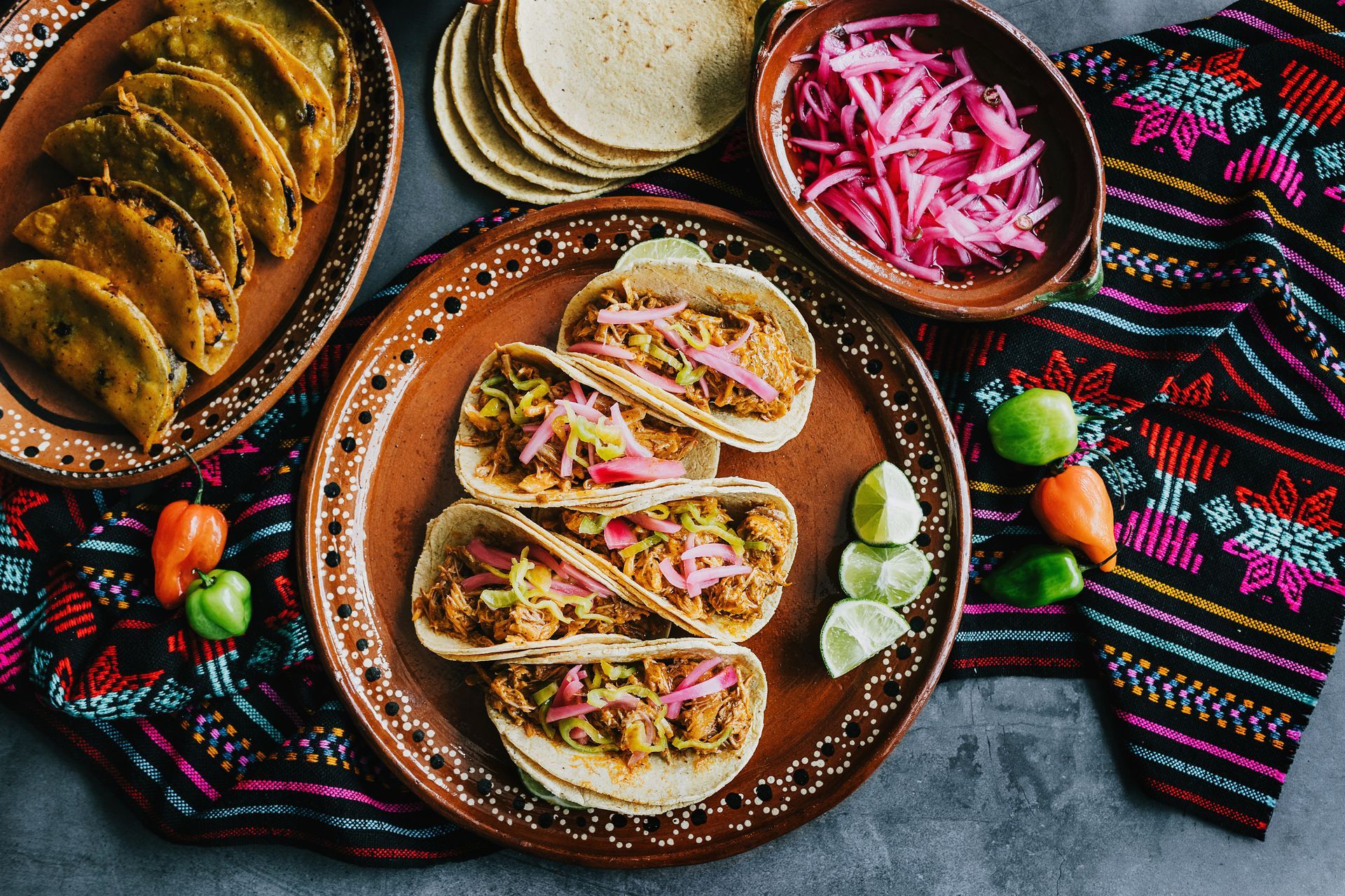 Tacos sur une assiette en terre cuite, garnis d'oignons roses marinés. Tortillas, citrons verts et poivrons sont également au menu.