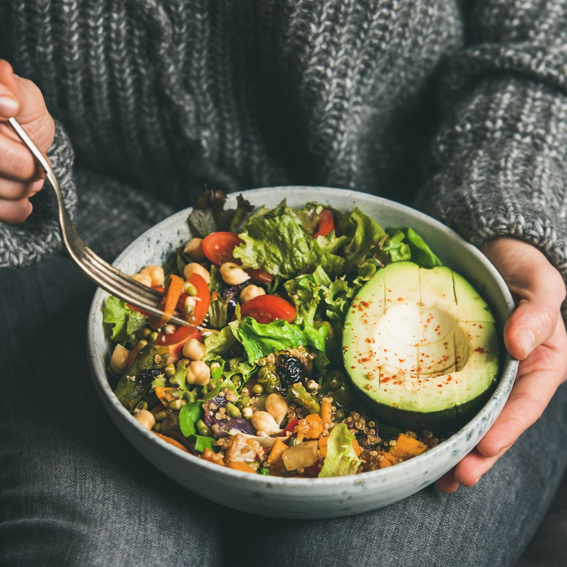 Personne mangeant une salade avec un demi-avocat, des haricots, des tomates et des légumes verts.