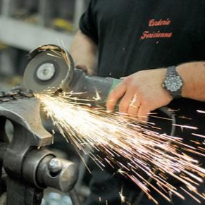 Une personne meule une chaîne métallique serrée dans un étau, créant des étincelles.