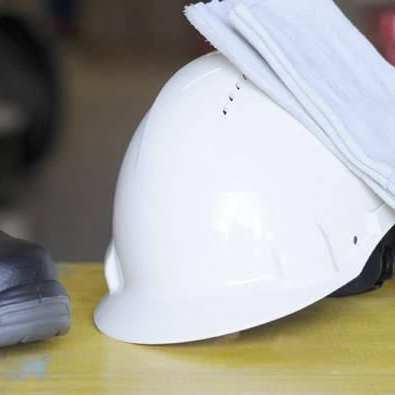 Casque de chantier blanc avec un tissu blanc plié dessus, à côté d'une chaussure noire.