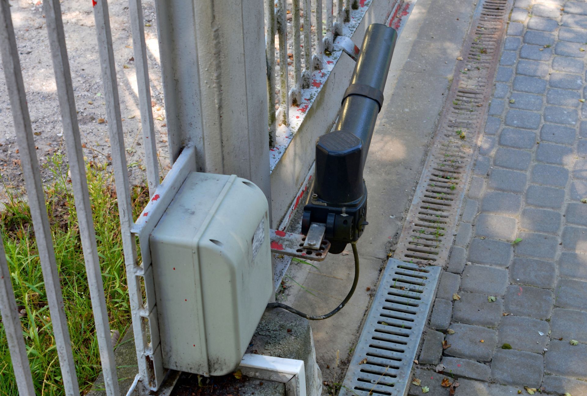 Caméra de surveillance noire fixée sur une clôture métallique à côté d'un chemin pavé.