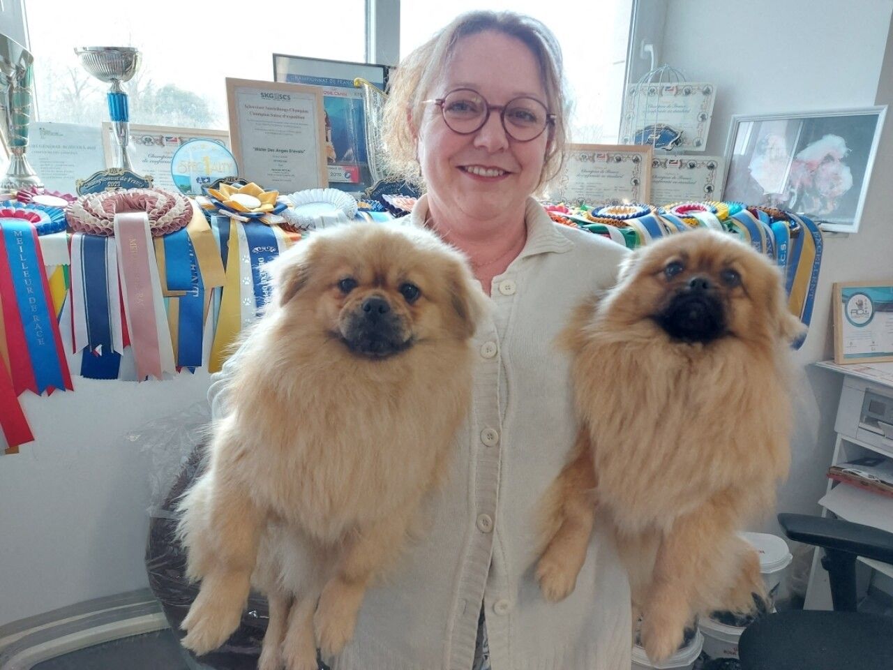 Madame Nicolas tenant ses deux épagneuls tibétains devant des médailles.