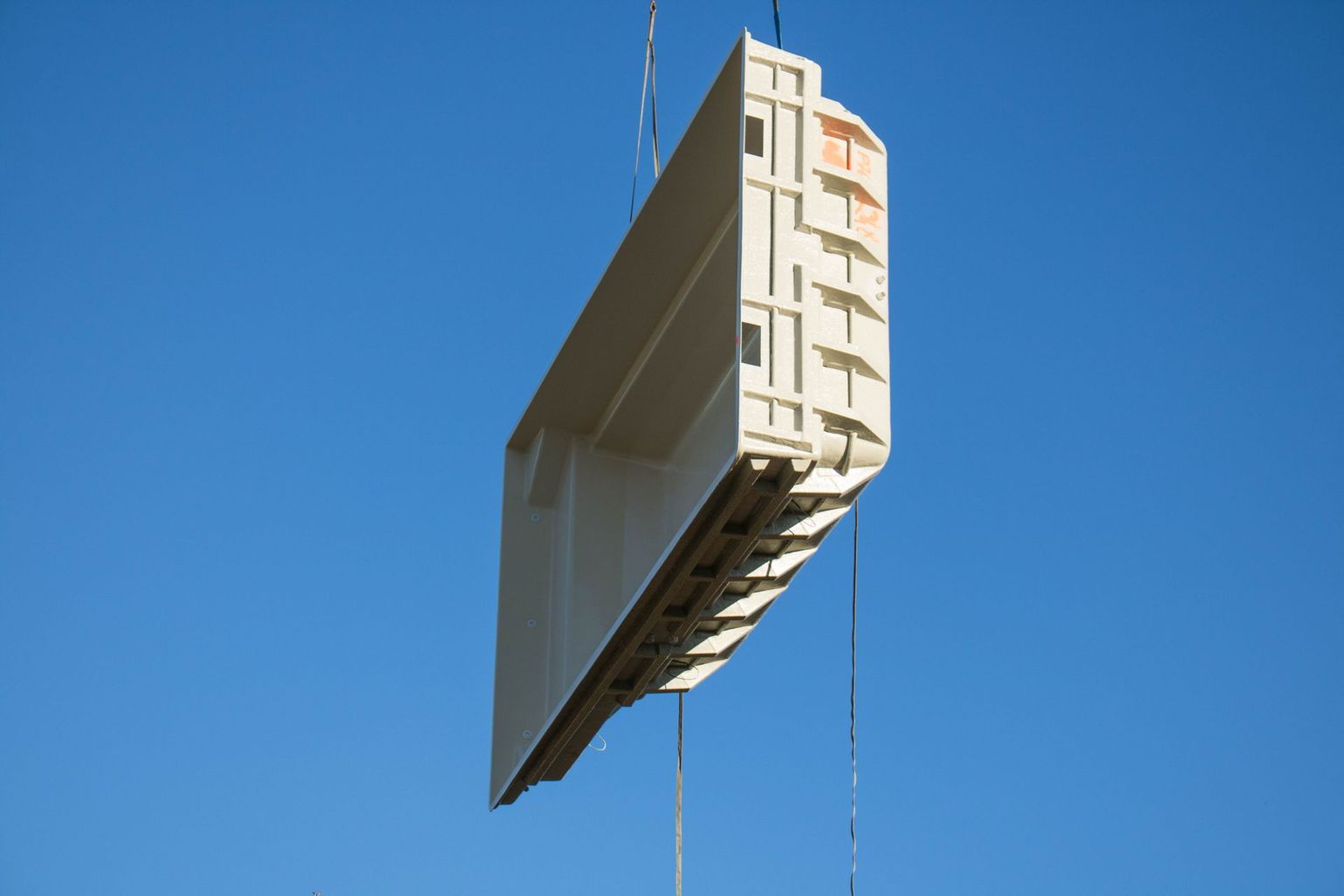 Un grand panneau mural en béton suspendu dans les airs contre un ciel bleu.