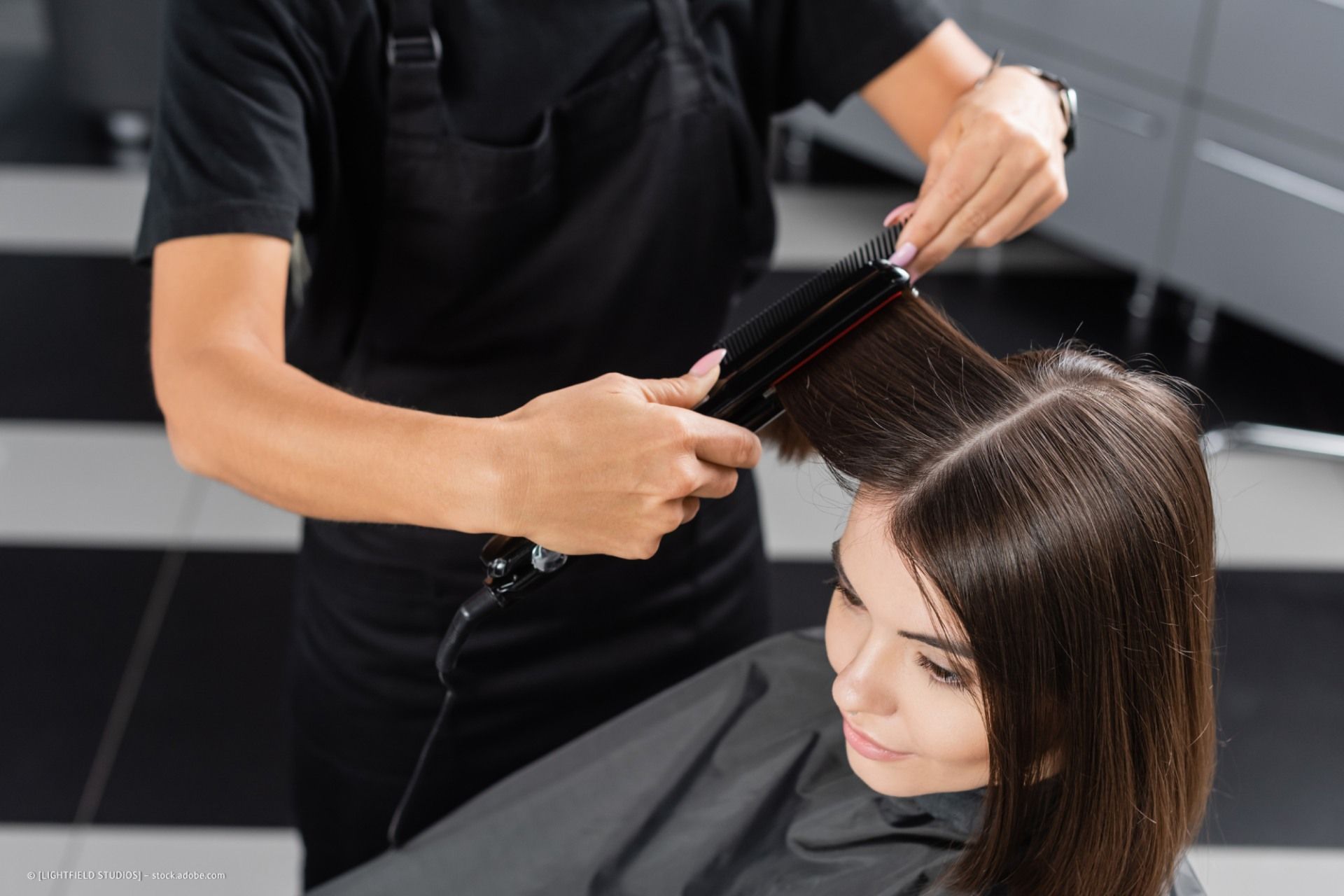 Friseur glättet in einem Salon das dunkle Haar einer Kundin.
