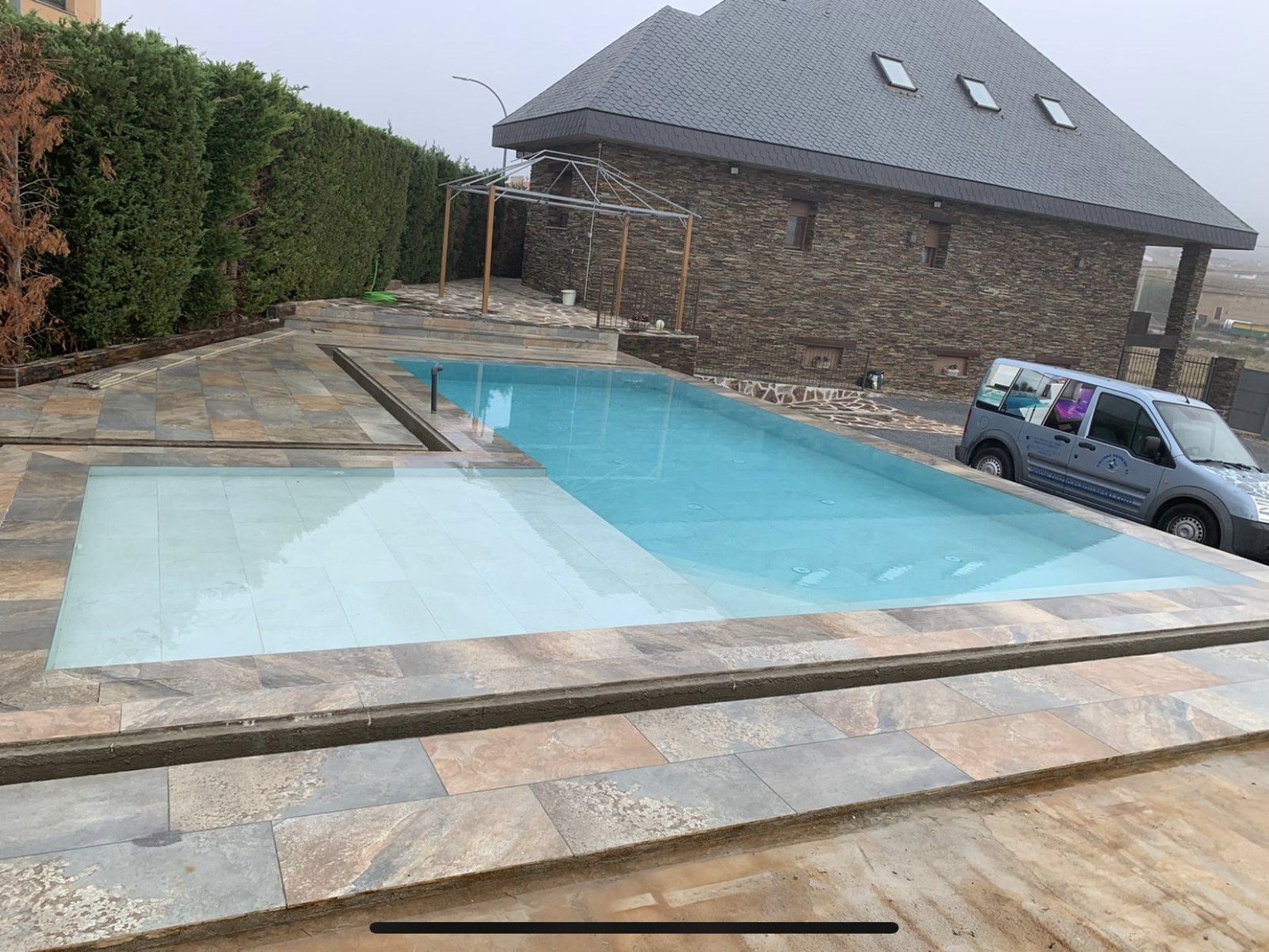 Un coche está aparcado junto a una gran piscina delante de una casa de piedra.