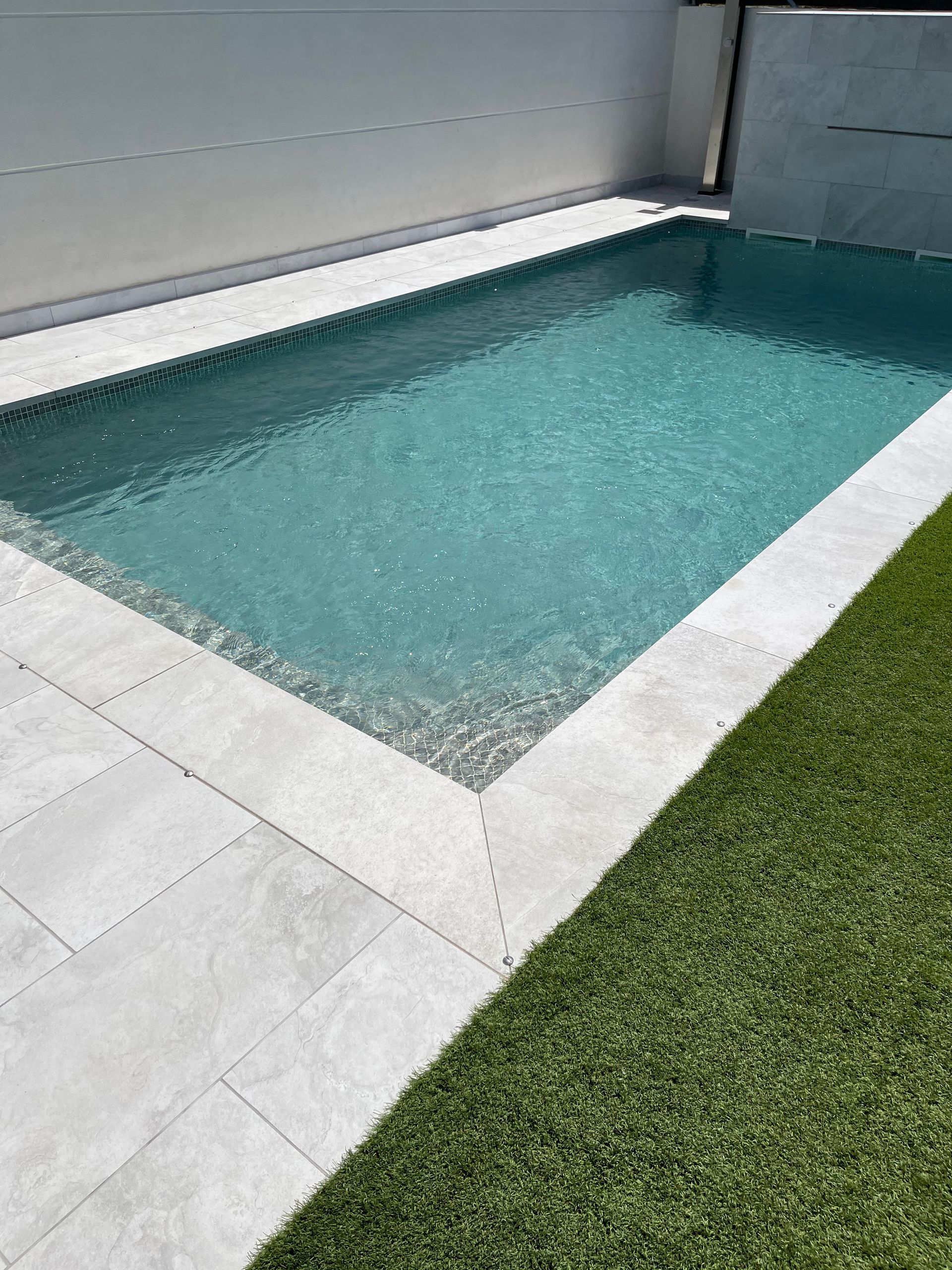 Una gran piscina rodeada de césped y azulejos en un patio trasero.