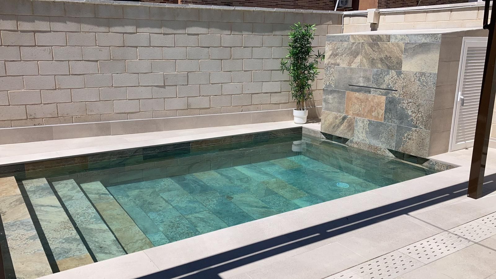 Una pequeña piscina con escaleras y una pared de ladrillos al fondo.