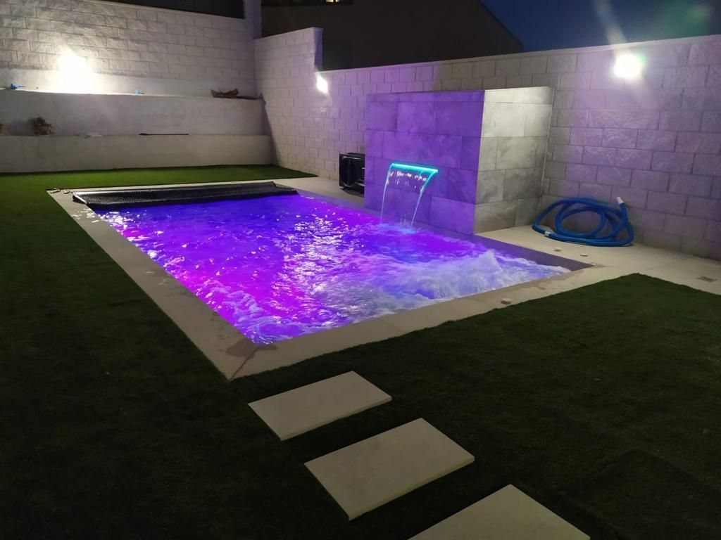 Una piscina con luces violetas y una cascada.