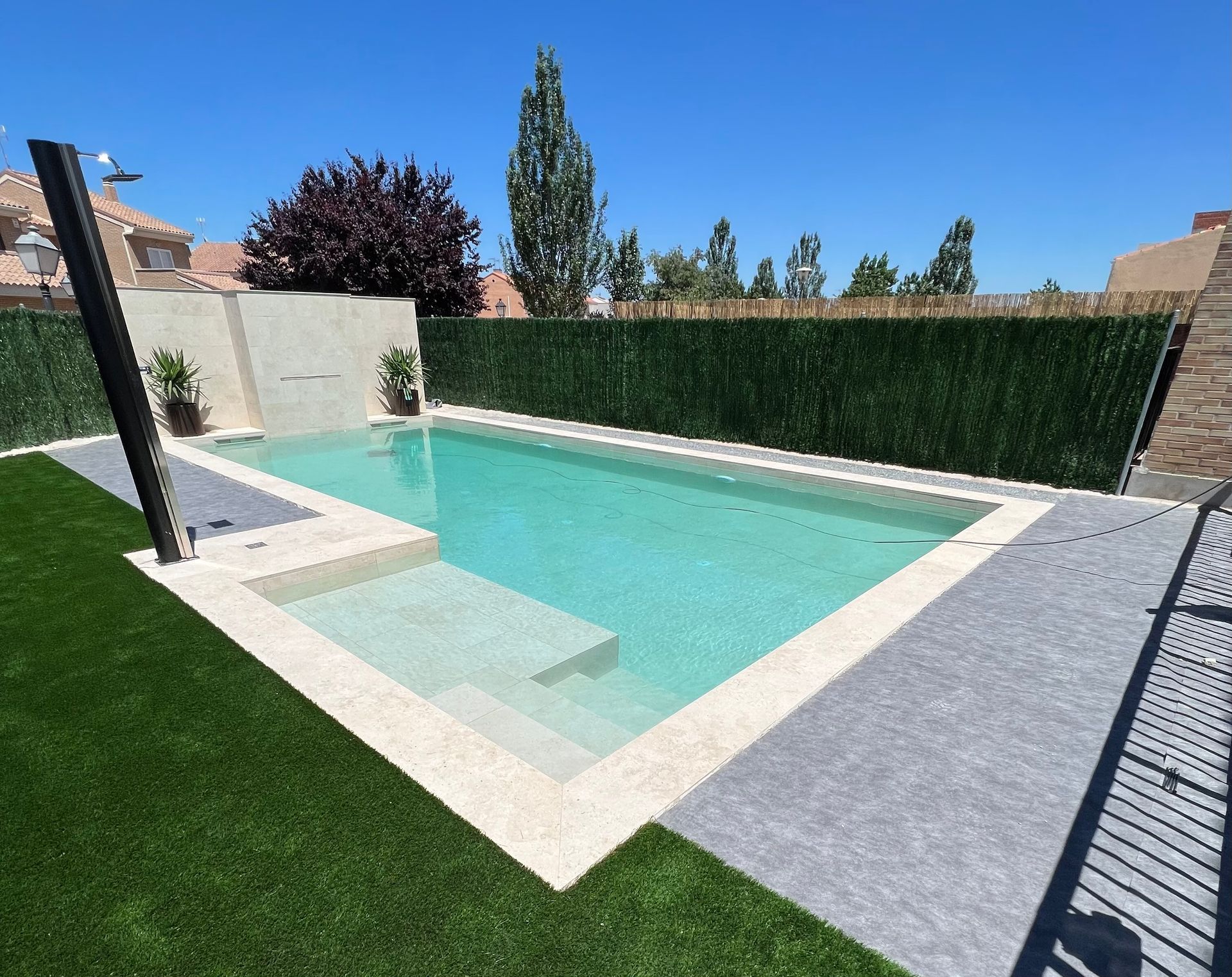 Una gran piscina está rodeada por un exuberante seto verde.