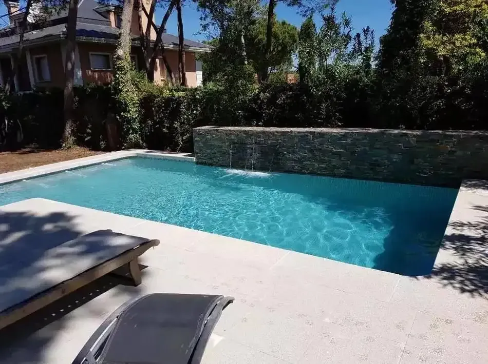 Una gran piscina está rodeada de árboles y una casa.