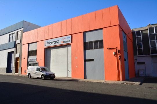 Una camioneta blanca está estacionada frente a un edificio naranja que dice Américas.