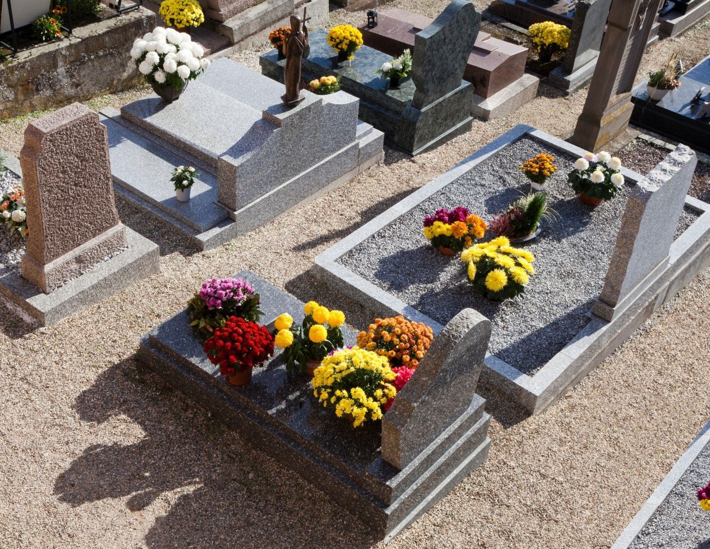 Lápidas en un cementerio, adornadas con coloridos arreglos florales y senderos de grava
