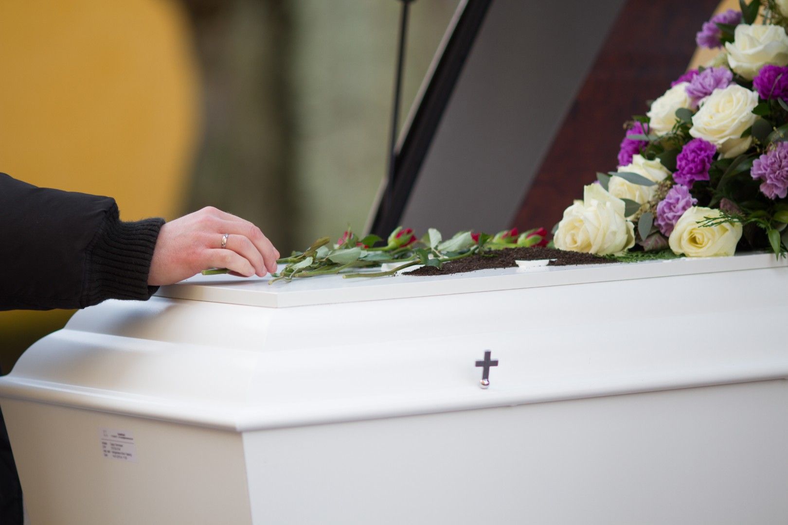 Una mano tocando un ataúd blanco adornado con flores en un funeral