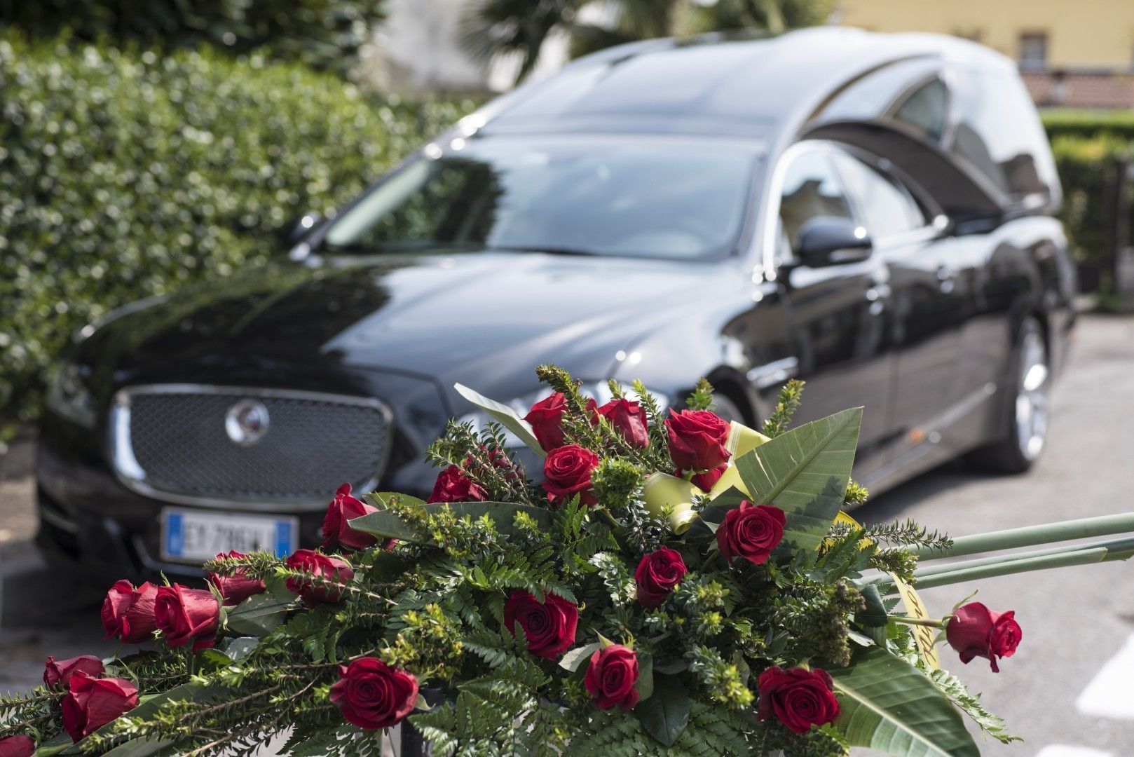 Un coche fúnebre negro detrás de una corona de rosas rojas en un funeral junto a la carretera