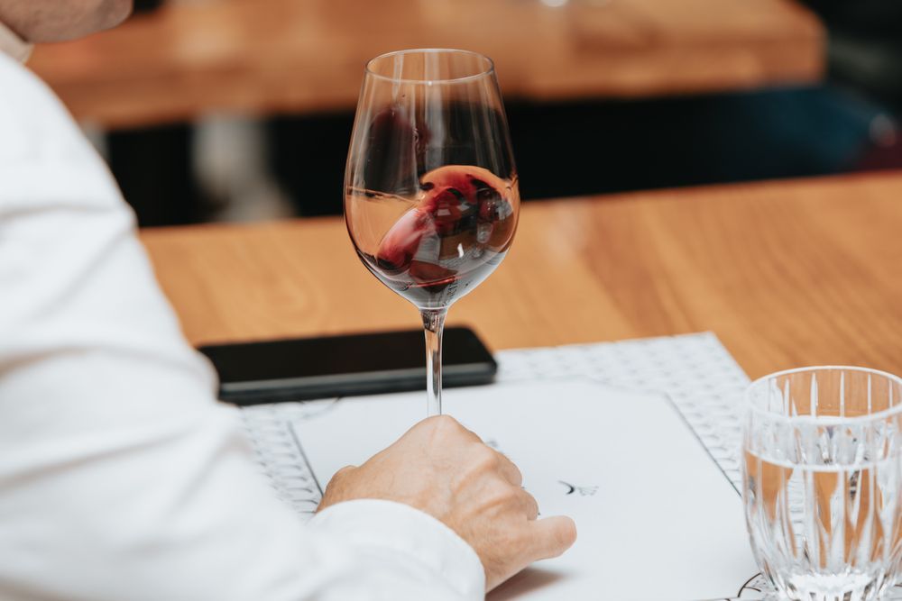 Una persona está sentada en una mesa sosteniendo una copa de vino.