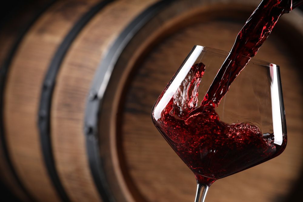 Se vierte una copa de vino tinto delante de un barril de madera.