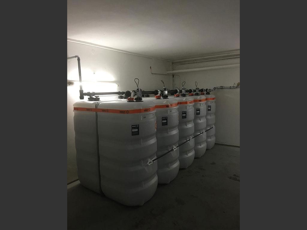 In einem dunklen Raum steht eine Reihe Plastikfässer aufgereiht.