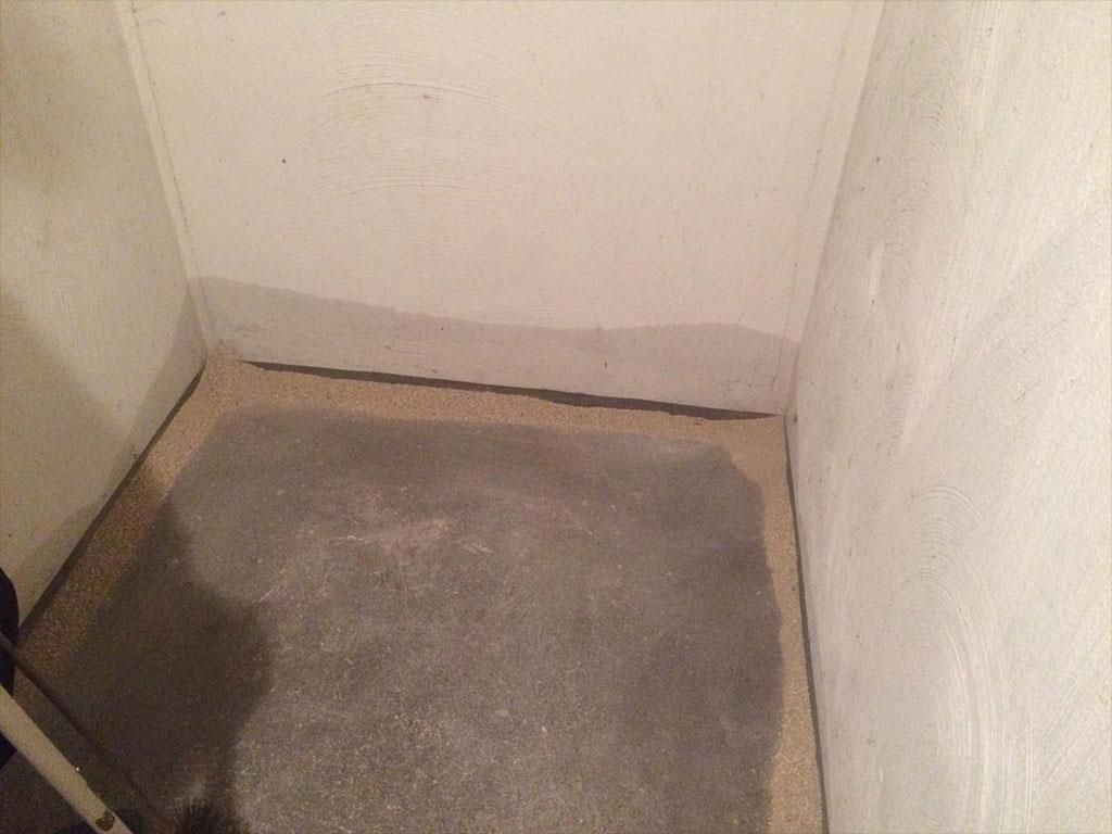 Eine Raumecke mit Betonboden und weißer Wand.