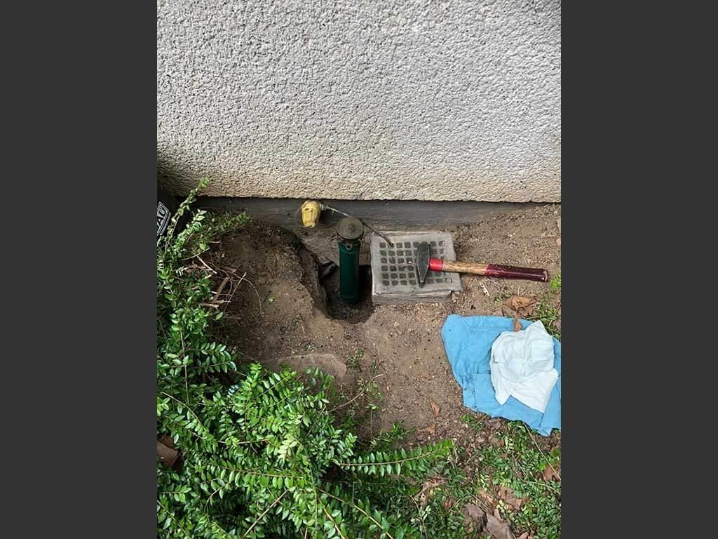 Mit Schaufel und Hammer ein Loch in den Boden neben einem Gebäude.