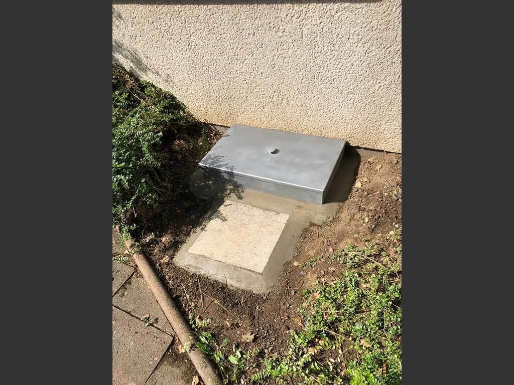 Eine Metallbox steht auf einem Betonblock im Dreck.