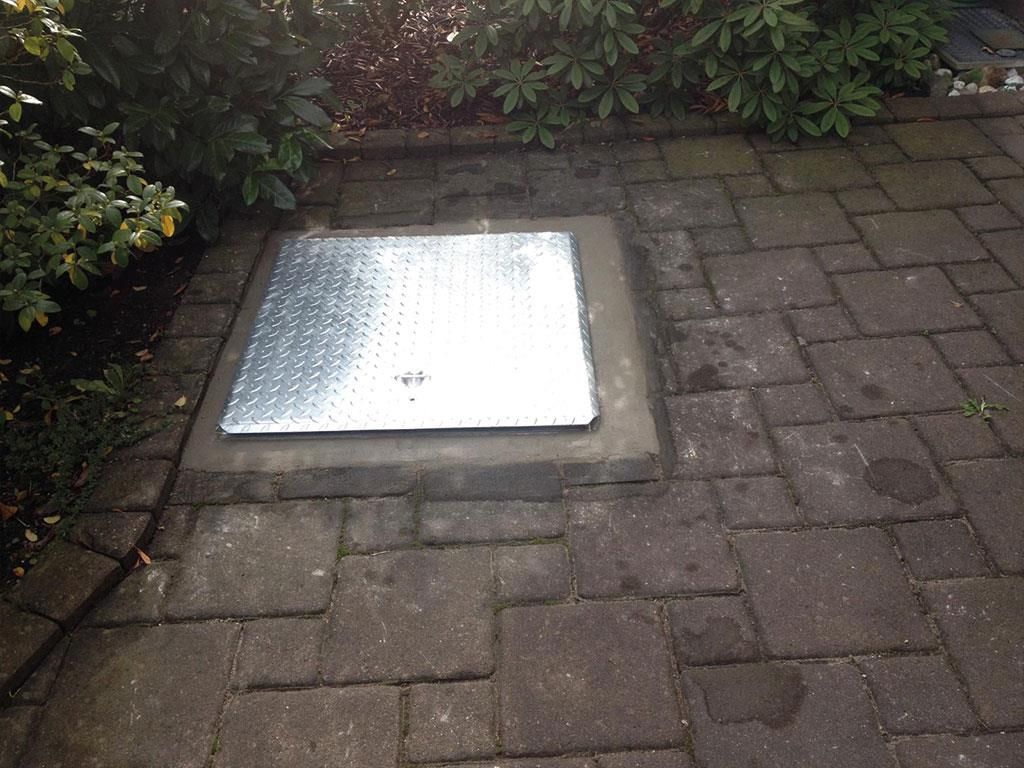 Eine Metallabdeckung liegt auf einem gemauerten Gehweg