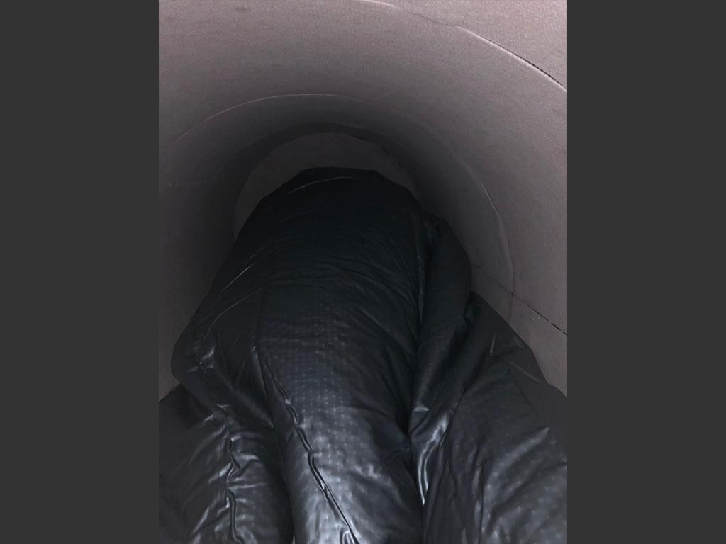 Eine Person liegt in einem schwarzen Sack in einem Tunnel.