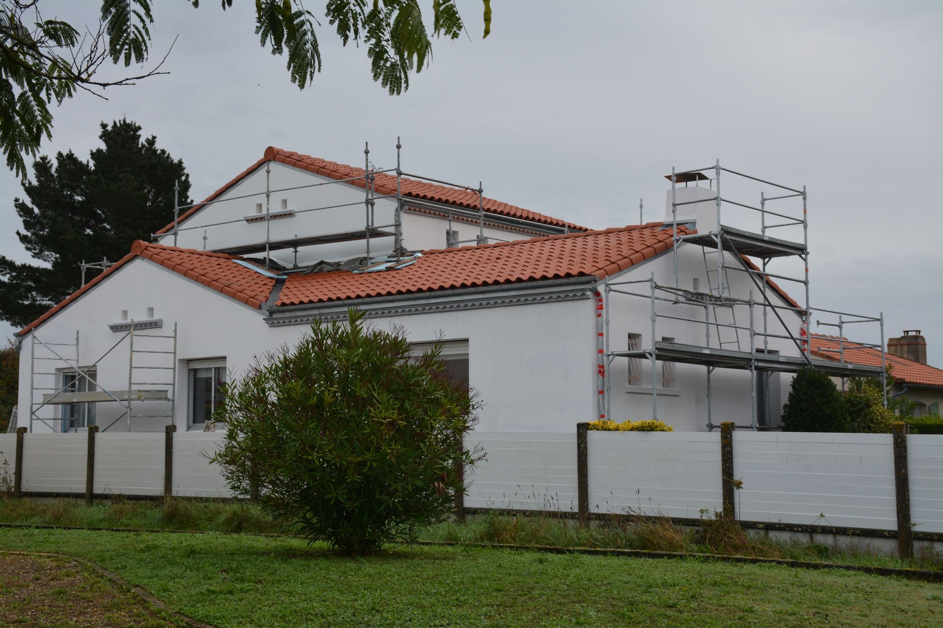 Maison aux murs blancs et au toit orange en cours de rénovation, avec des échafaudages.