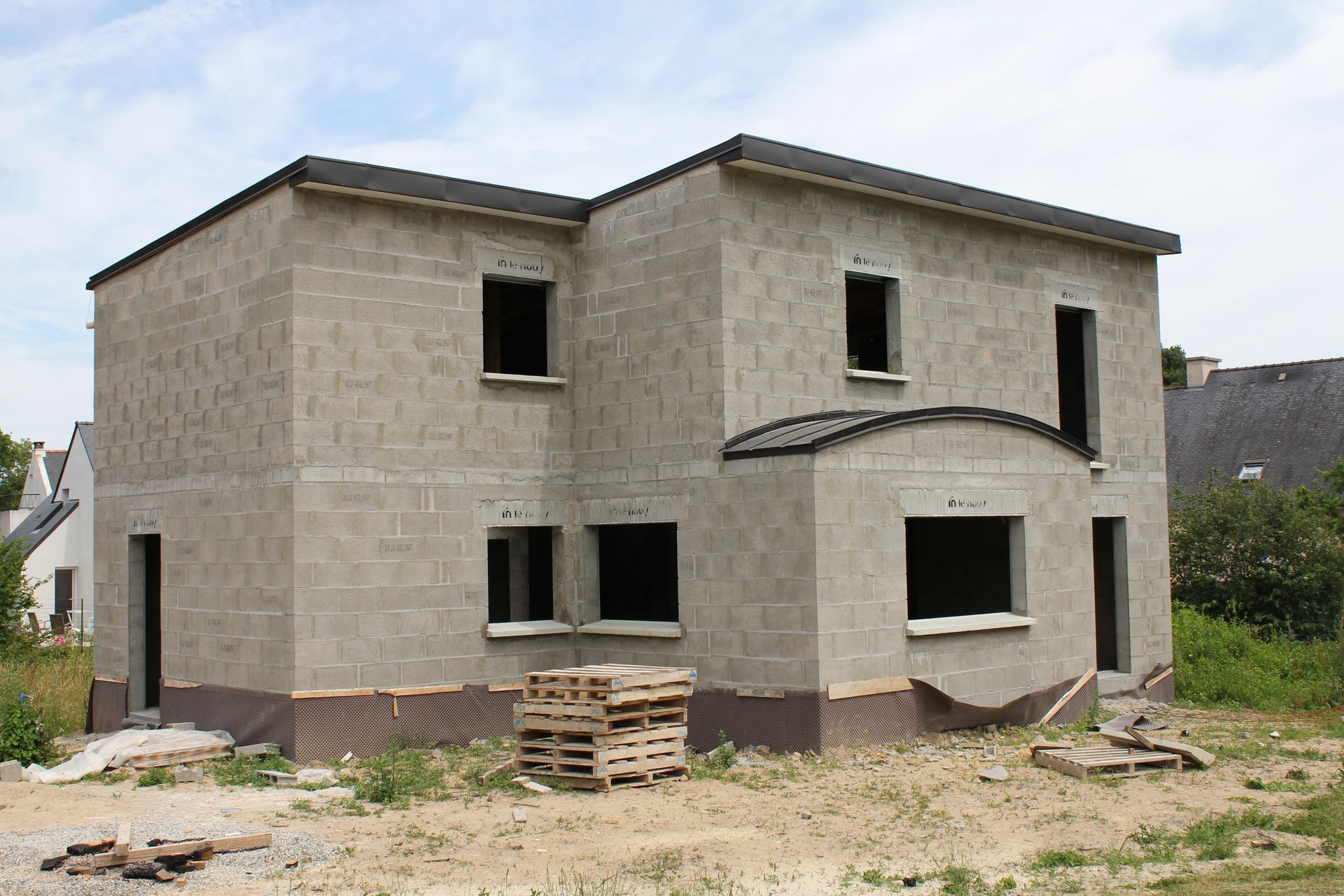 Maison inachevée de deux étages en parpaings gris. Les fenêtres et l'entrée arrondie sont vides.