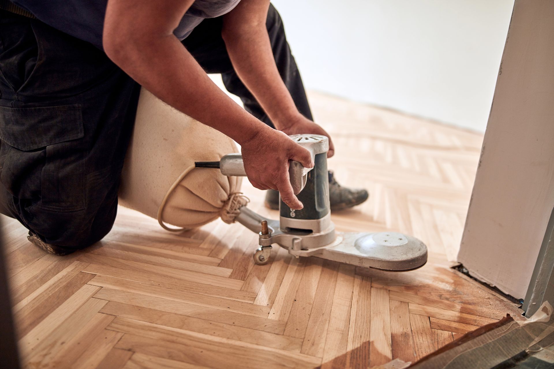 Personne agenouillée, utilisant une ponceuse à parquet pour rénover un plancher en bois dur.