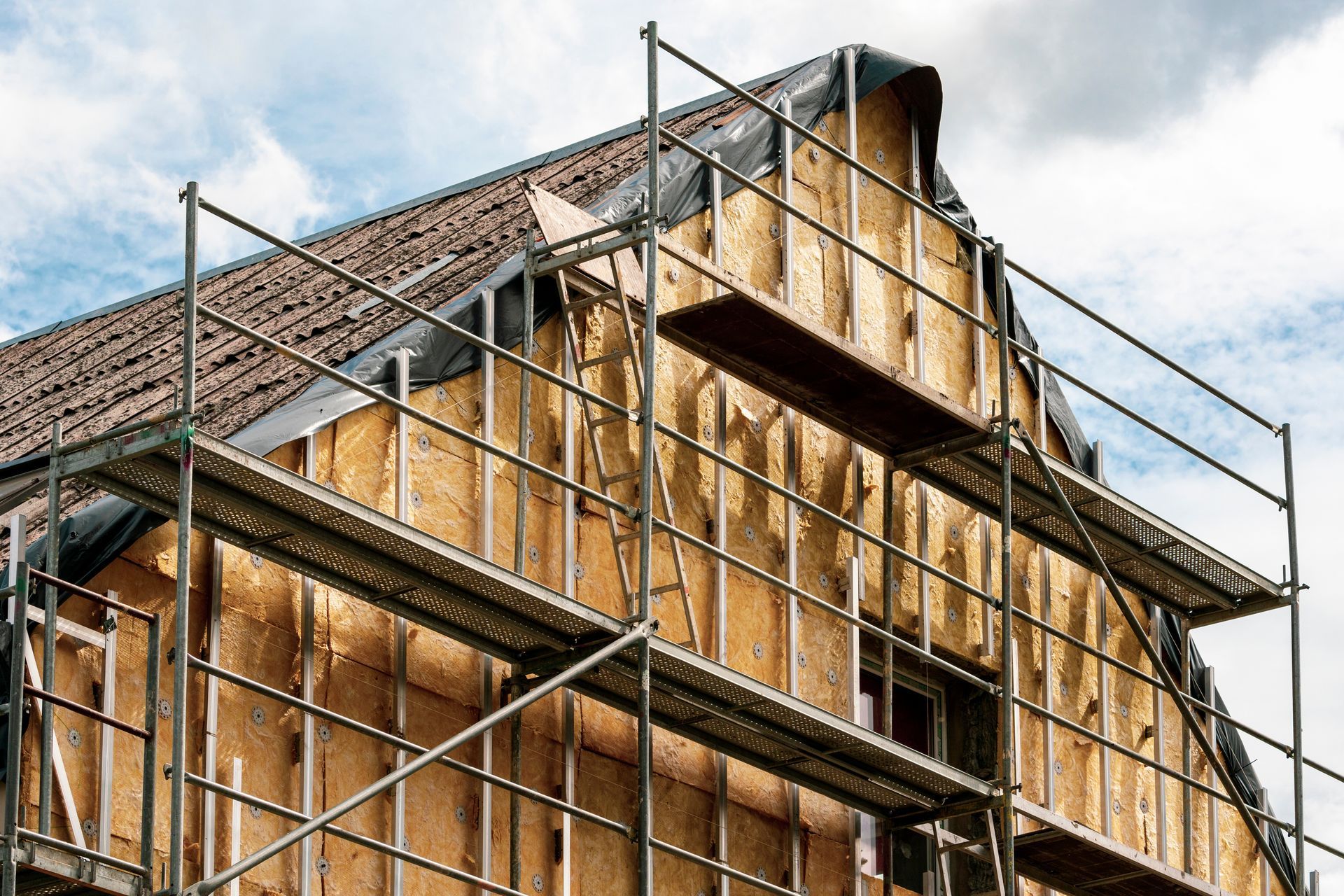 Bâtiment en construction, échafaudages autour du pignon, isolation apparente, bâche sombre sur le toit.
