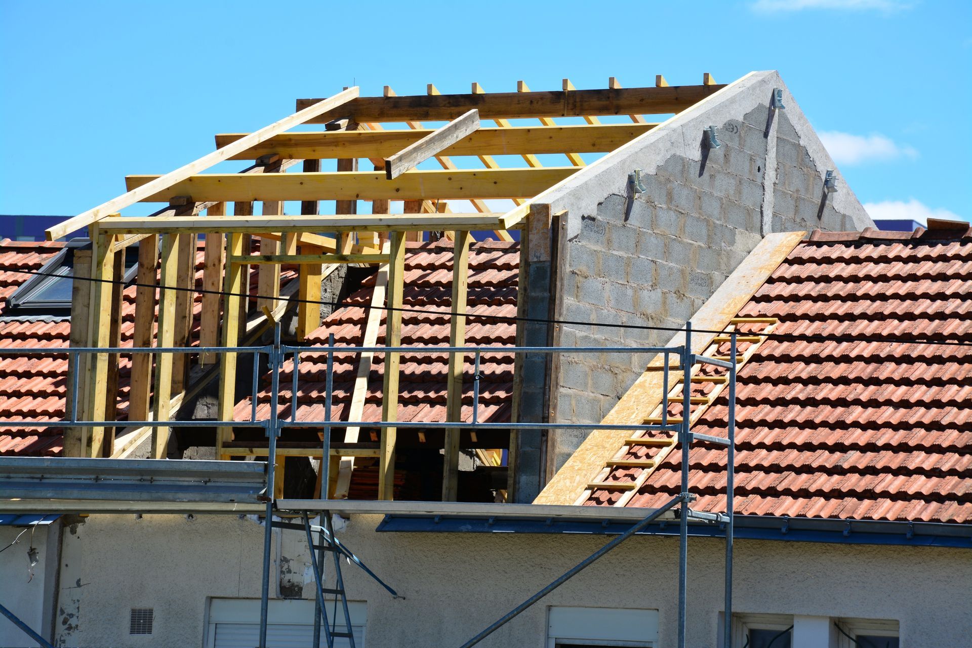 Construction de la toiture : charpente d’une lucarne sur un toit de tuiles. Des échafaudages sont visibles.